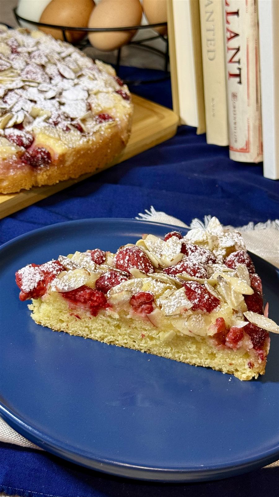 A slice of raspberry almond cake topped with sliced almonds and powdered sugar