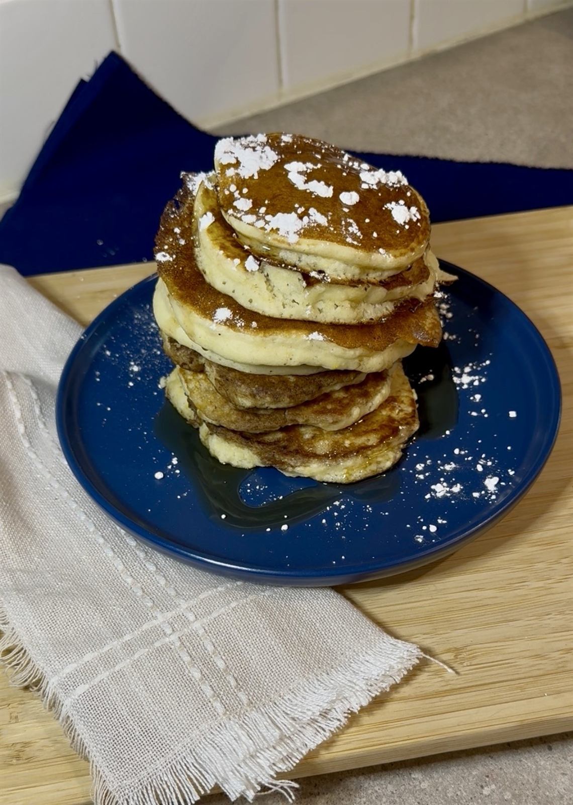 A stack of sourdough pancakes dusted with powdered sugar and drizzled with syrup
